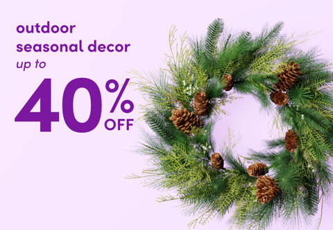 Outdoor seasonal decor up to 40 percent off, featuring a lush evergreen wreath decorated with pinecones against a light purple background.