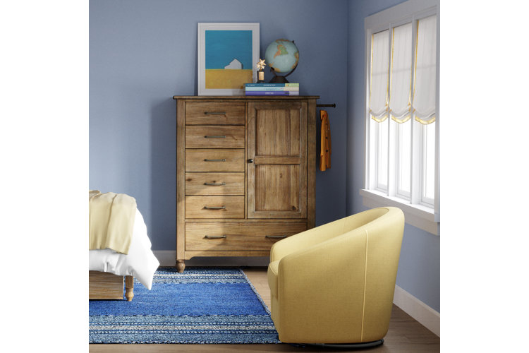 A rustic wood chifforobe featuring multiple drawers and a cabinet door in a boho-style room with blue walls and a yellow accent chair