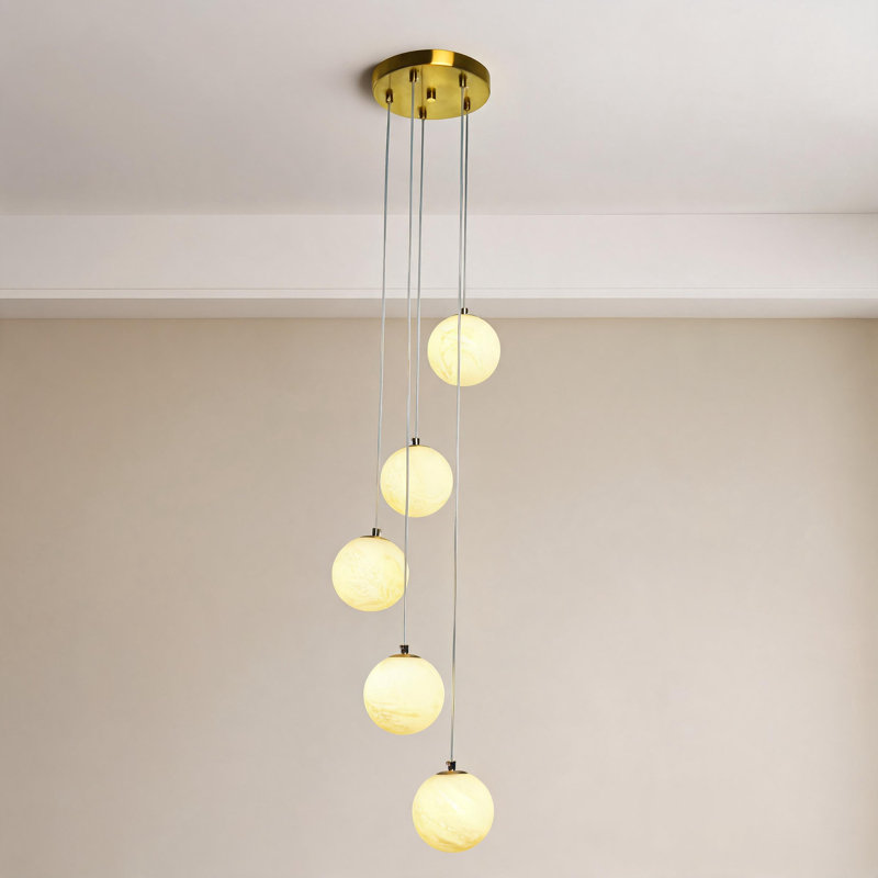 Suspension moderne à 5 lumières avec globes en verre imitation albâtre et finition laiton.