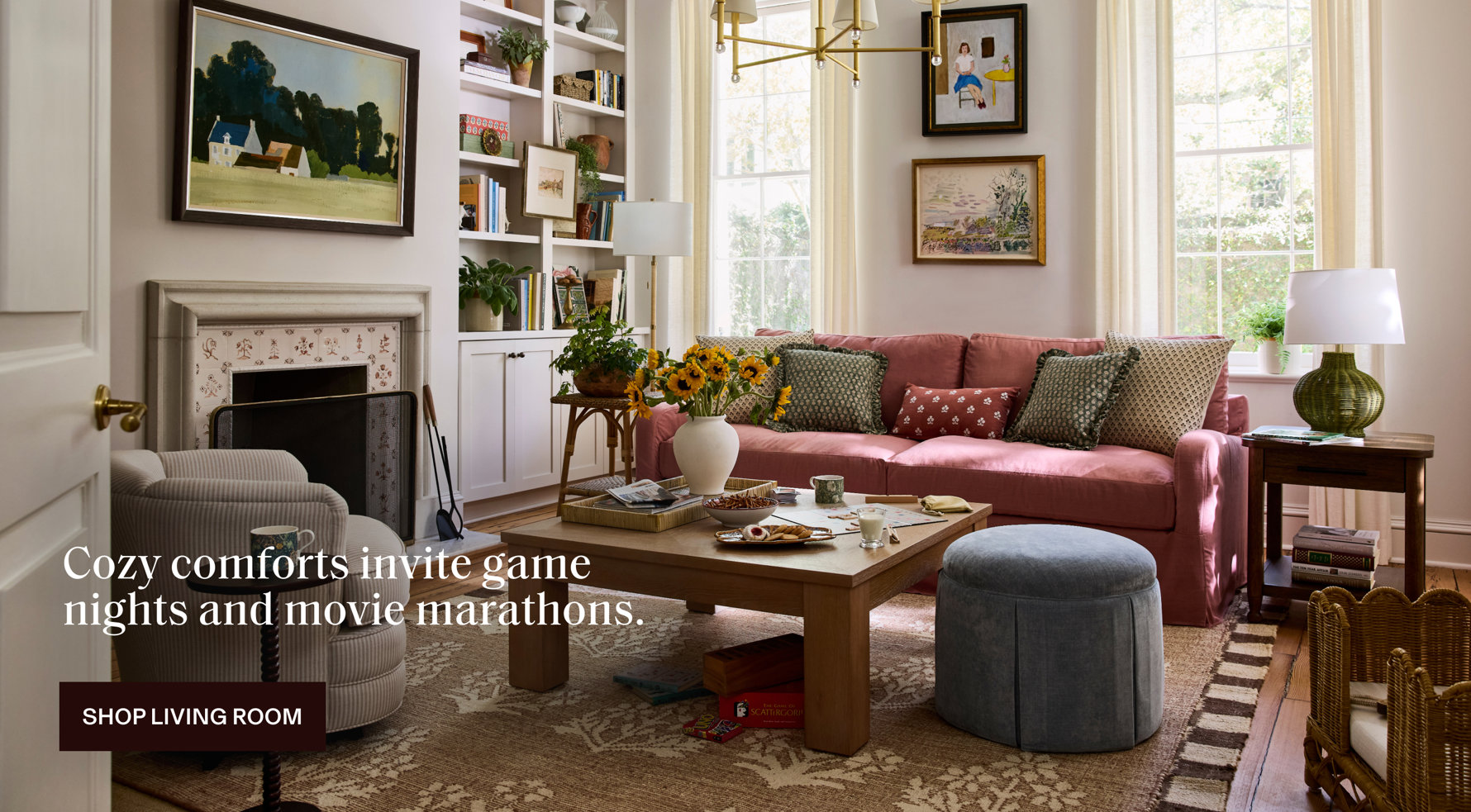 Cozy living room with a rose-colored sofa, fireplace, and patterned rug with text overlay that reads: Cozy comforts invite game nights and movie marathons. SHOP LIVING ROOM.
