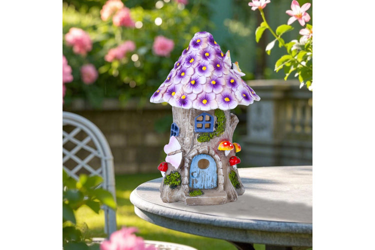 resin fairy home on a stone garden table surrounded by pink flowers