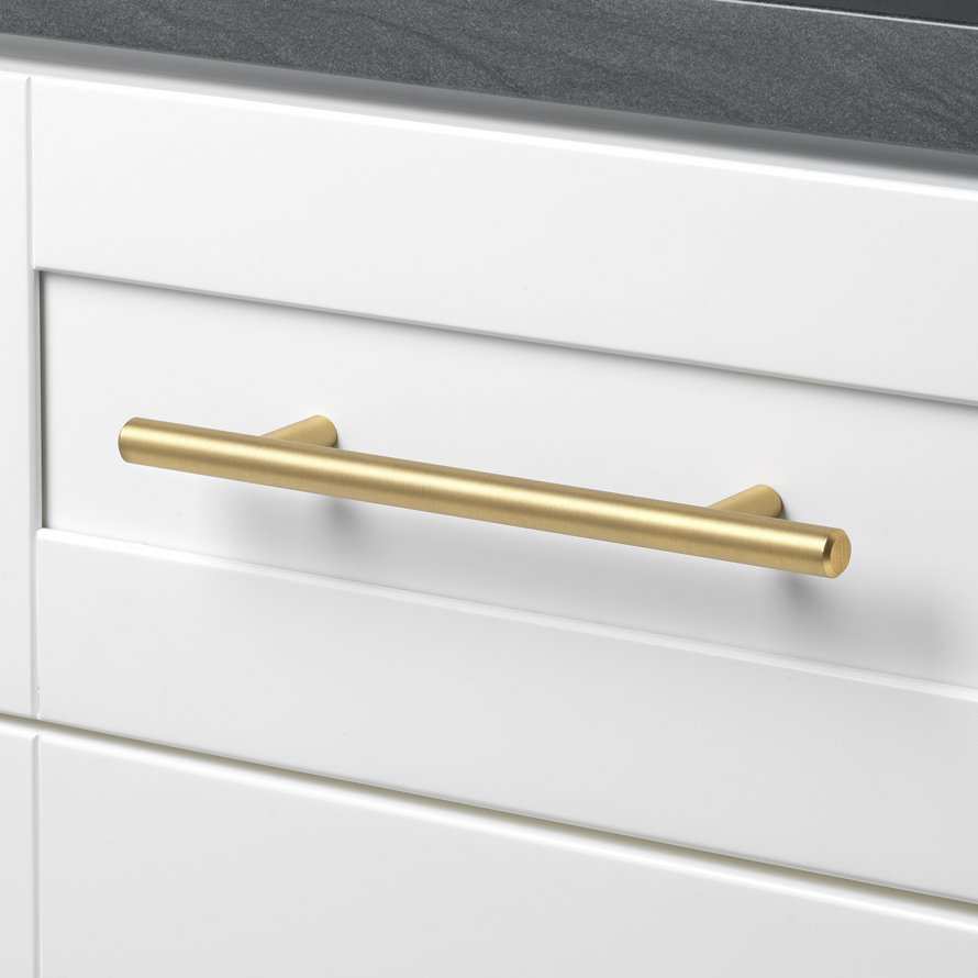 Brushed gold bar drawer pull mounted on a white shaker-style cabinet drawer.