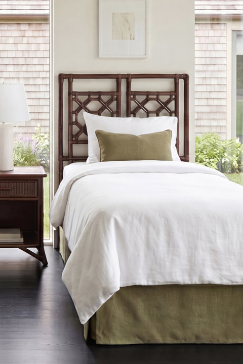 Twin bed featuring a dark wood bamboo-style headboard, white bedding, an olive green lumbar pillow, and a matching olive green bed skirt.