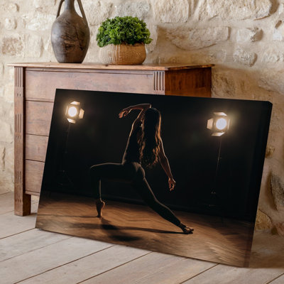 Toile, une gracieuse danseuse se tient dans un studio peu éclairé faisant face à un art mural éloigné du spectateur présentant une pose puissante