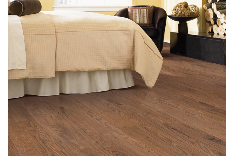 medium brown wood laminate flooring in a bedroom with a bed with a yellow and white bed spread and a stack of wood for a fire