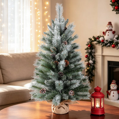 Arbre de Noël floqué sur table avec pommes de pin et base en toile de jute