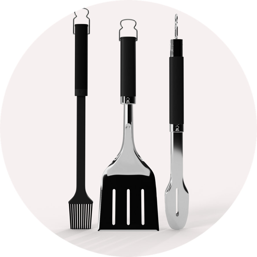 Set of three stainless steel grilling tools featuring black ergonomic handles, including a basting brush, spatula, and tongs.