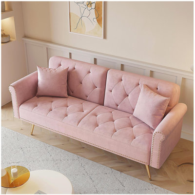 Un canapé-lit de 69,7 pouces de long recouvert de velours rose, équipé de décorations à têtes de clous et de coussins décoratifs assortis