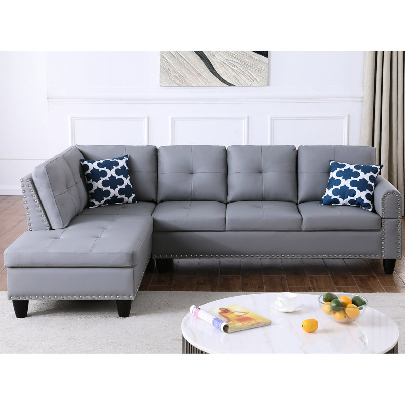 Canapé d'angle en L 3 pièces en similicuir gris, idéal pour des séances de cinéma et des jeux vidéo relaxantes. Siège central rabattable avec porte-gobelets, deux coussins décoratifs et rangement. Structure en bois massif et composite, profil bas.