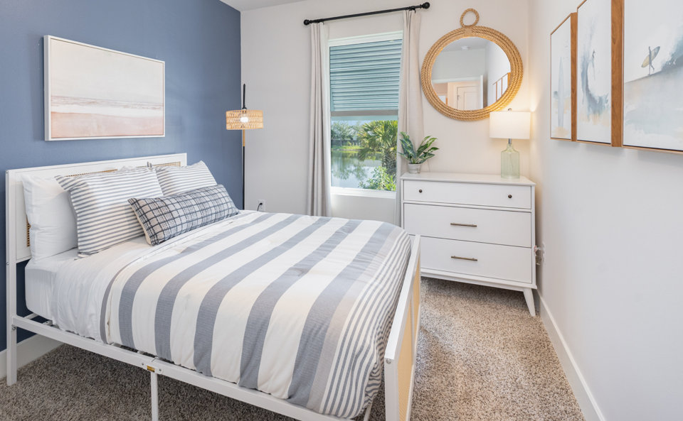 Bedroom with blue accent wall, bed with striped comforter, and white dresser.