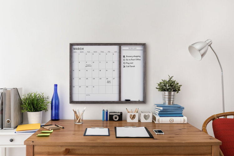 whiteboard calendar hanging over a wood desk in a home office