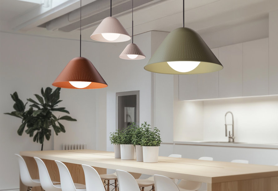 Four modern pendant lights with perforated shades in various colors hanging above a wooden dining table in a bright kitchen.