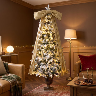 Sapin de Noël enneigé avec des pommes de pin naturelles et un nœud doré au sommet