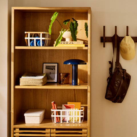 Shelves with basket, books, lamp, and potted plant, next to wall hooks with bag and hat