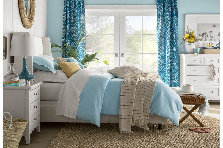 coastal-style bedroom with bright teal, geometric-patterned curtains framing French doors