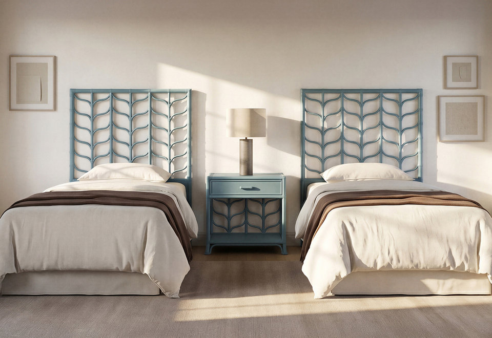Two twin beds with blue leaf-patterned headboards and white bedding sit on either side of a matching blue nightstand with a lamp in a sunlit bedroom.