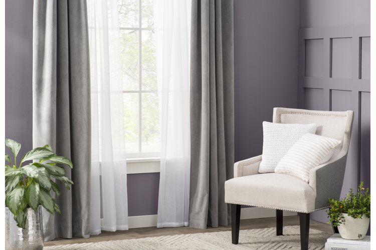 layered room-darkening and light-filtering curtains in a room with purple walls and a gray accent chair