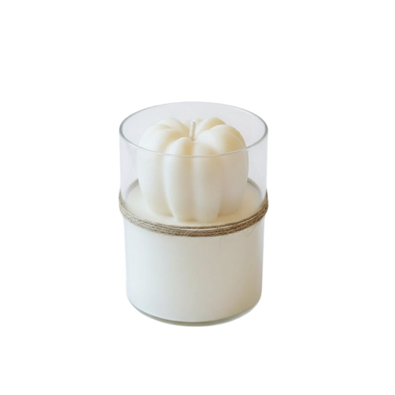Bougie miniature parfumée à la citrouille et à la pomme, couleur ivoire, dans un pot en verre transparent.
