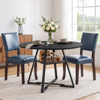 Ensemble table et chaises de salle à manger : table ronde industrielle de 119 cm avec pieds croisés et étagère de rangement en maille, et chaises de salle à manger en bois rembourrées de style milieu du siècle.