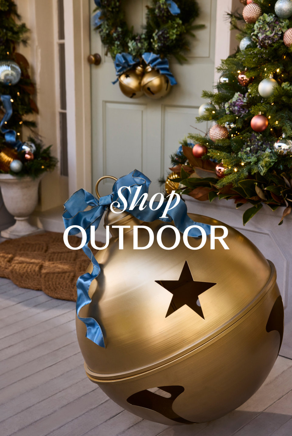 Large gold metal bell ornament with a blue ribbon on a festive front porch decorated for the holidays with the text Shop OUTDOOR.