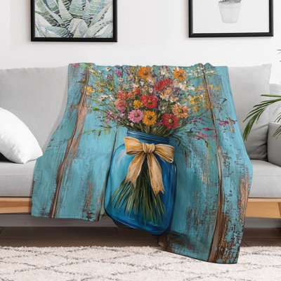 Jeté de fleurs sauvages dans un pot Mason bleu contre une luxueuse jeté en flanelle de bois, couverture douce et chaude pour le canapé-lit du salon