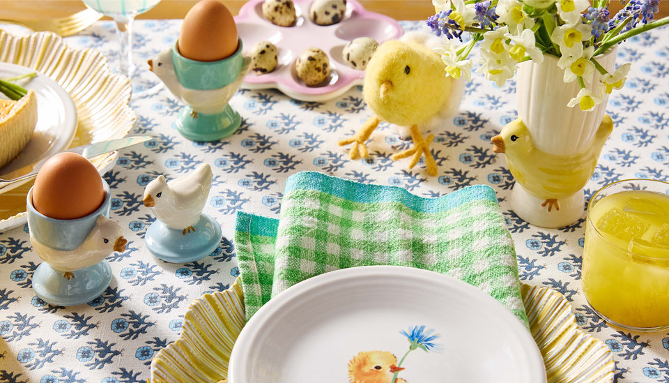 Mise en table de Pâques avec coquetiers, œufs de caille, fleurs, et un poussin tenant une fleur sur une assiette.