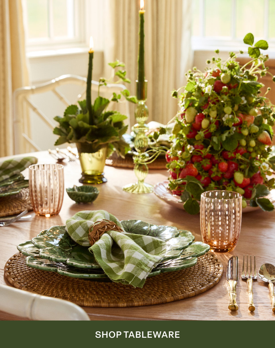 Elegant table setting with green gingham napkin, wicker charger plate, glassware, and seasonal fruit centerpiece with Shop Tableware button