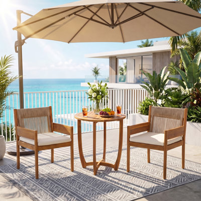Ensemble bistro de patio Celia pour 2 personnes, style côtier moderne, en bois d'acacia, avec fauteuils à accoudoirs tressés, coussins et table ronde à lattes.