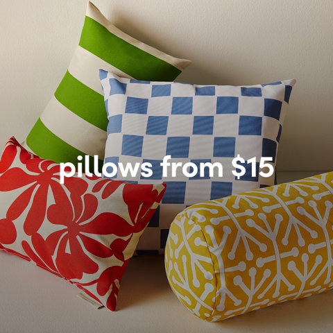 A stack of colorful outdoor pillows in green stripes, blue checkers, red florals, and yellow patterns from $15.