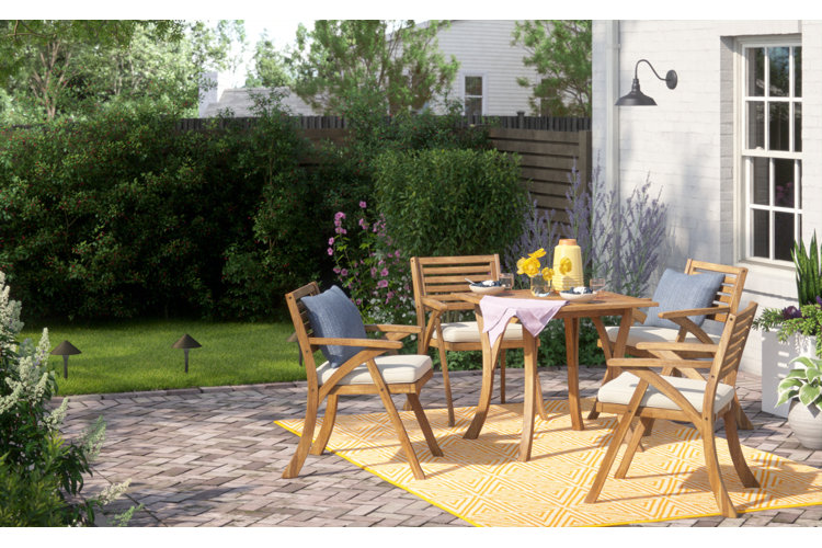 outdoor patio with a yellow rug and wooden dining set framed by landscaping path lights