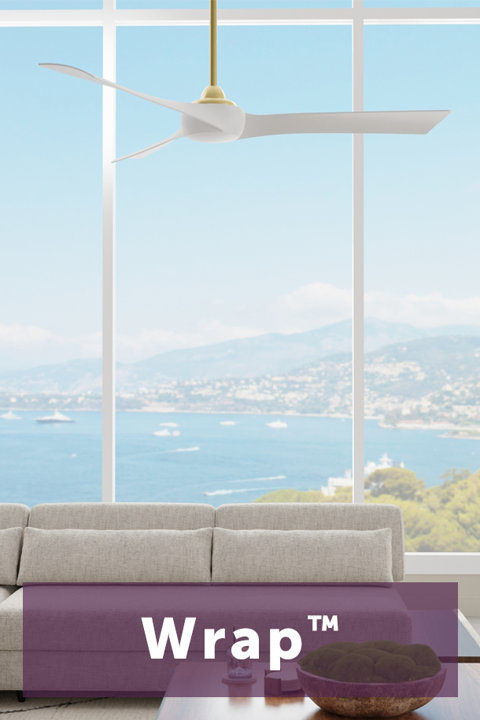 Modern ceiling fan with white blades and brass hardware centered in front of a large window overlooking a coastal view with a beige sofa in the foreground and the text Wrap centered at the bottom.