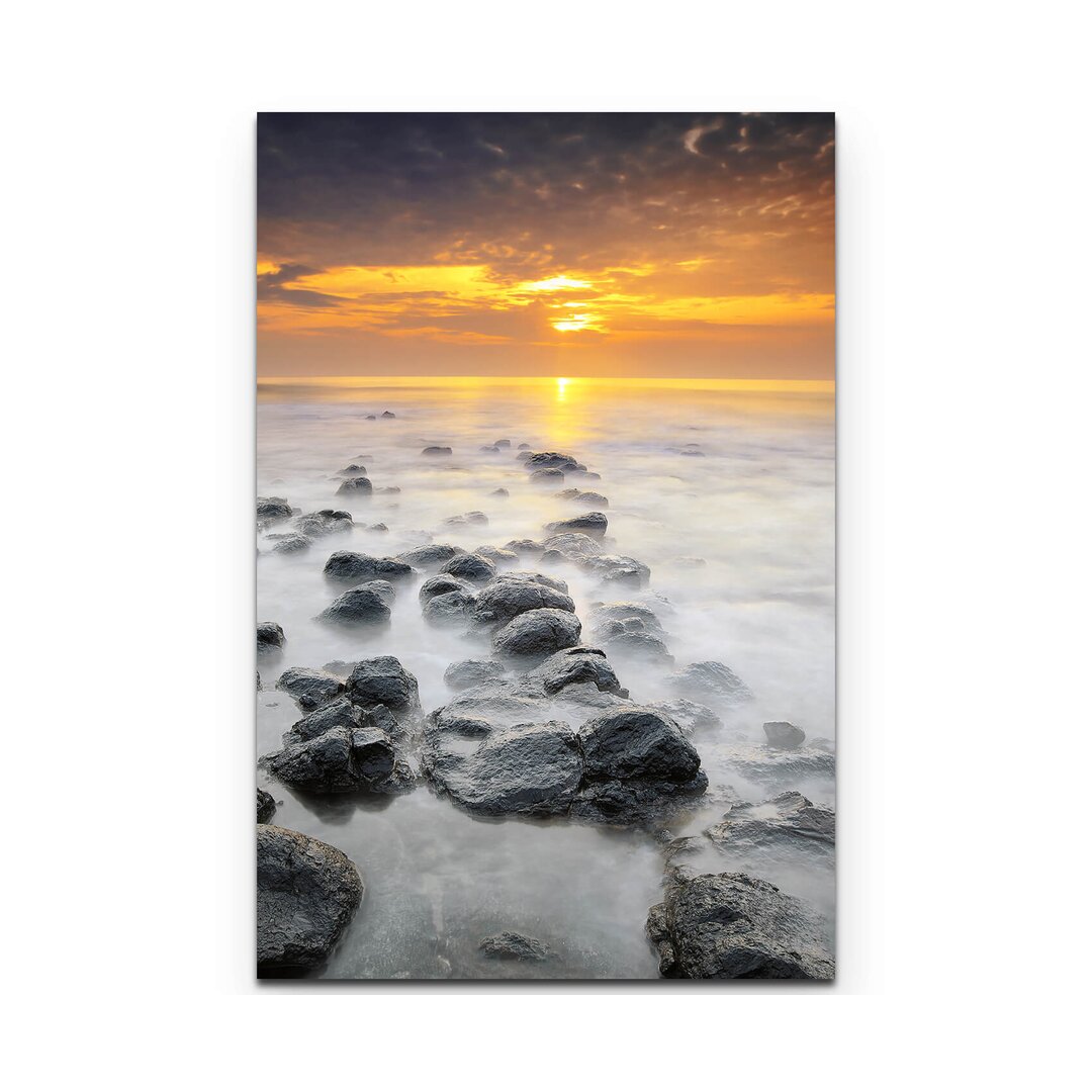 Leinwandbild Sonnenaufgang über einem Strand mit schwarzen Steinen