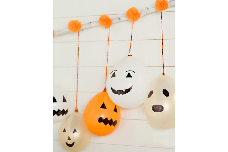 Jack-o'-Lantern balloons hanging from a wooden stick with paper pom poms