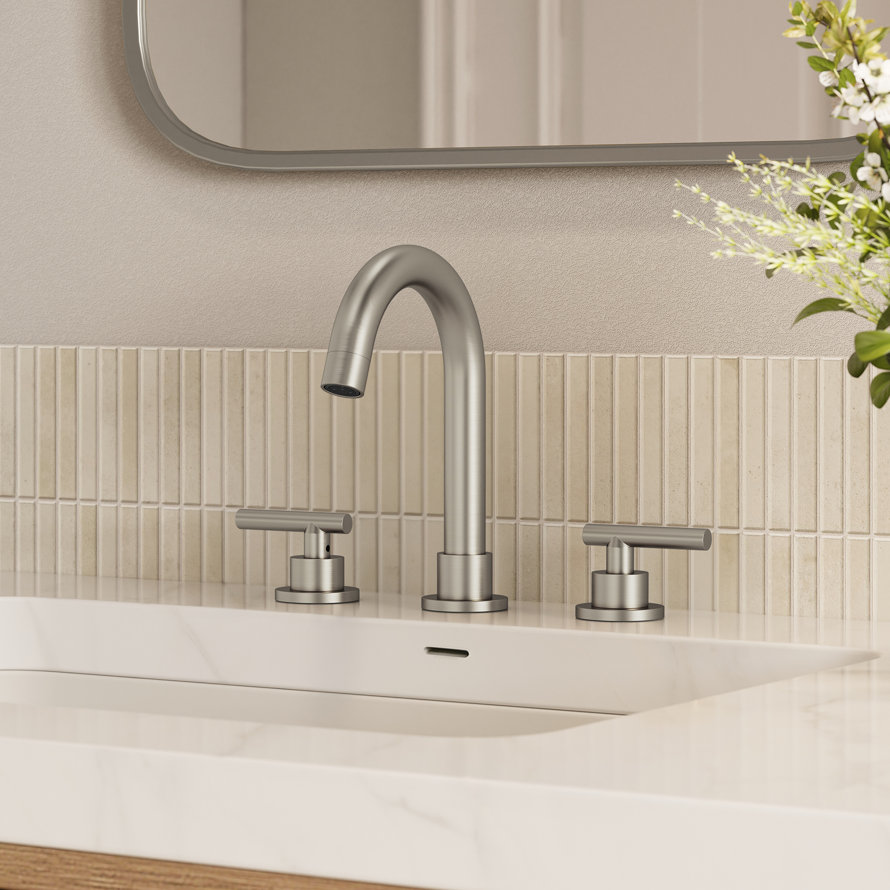 Modern brushed nickel widespread bathroom faucet with two lever handles mounted on a white marble vanity countertop against a vertical tile backsplash.