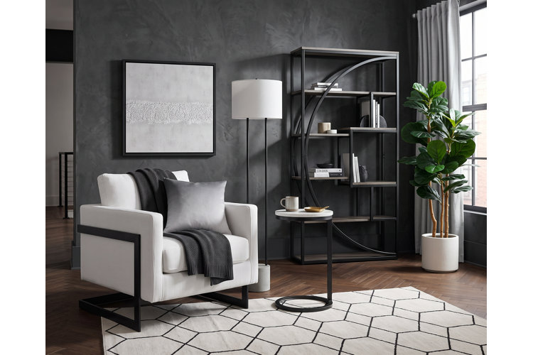 Modern industrial living room with a white accent chair, black and white geometric area rug, dark gray limewashed walls, and a matte black metal etagere bookcase.