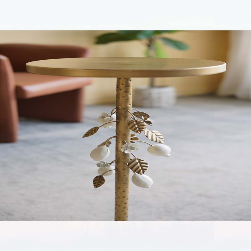 Table d'appoint ronde en fer avec accents floraux dorés et blancs, base en ciment et détails botaniques élégants pour les intérieurs modernes