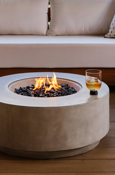 Round fire pit with glass and sofa in background.