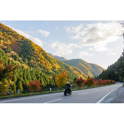 A Motorcycle Running On The Road Facing The Autumnal Mountains by Komta - Wrapped Canvas Print
