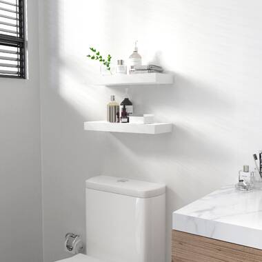 White stacked floating shelves are mounted in a nook above a drop in bathtub  fitted with a white subway tile…