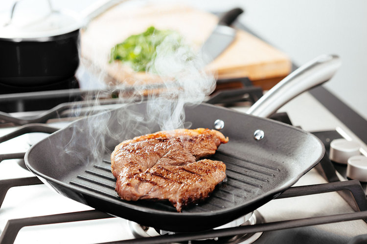 A cast iron grill pan with a steak cooking in it