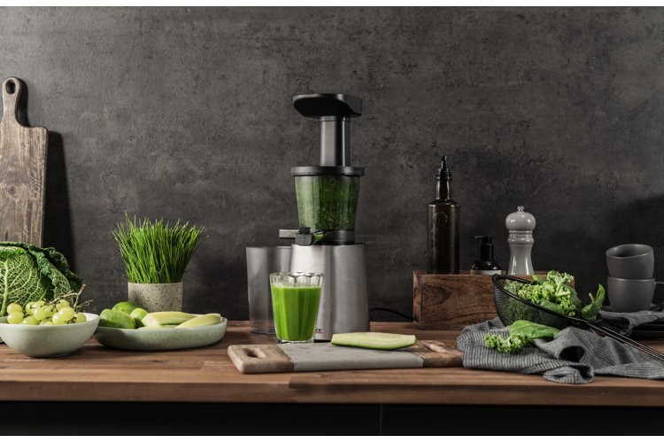 modern kitchen with a gray wall and wood countertop filled with a cold press juicer, cutting board, and a range of fruit and vegetables to be squeezed
