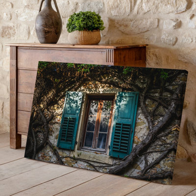 "Toile", une fenêtre en bois patinée avec des volets sarcelle partiellement fermés est un ensemble d'art mural sur fond de murs de pierre en ruine