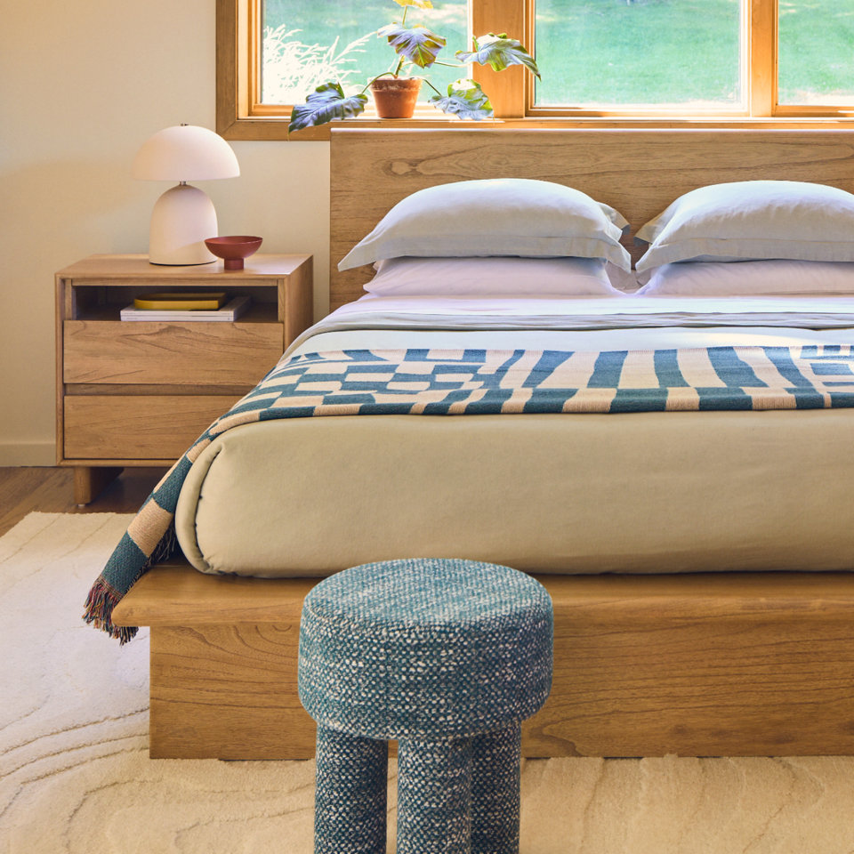 Bedroom with wood bed, nightstand, lamp, and blue stool.