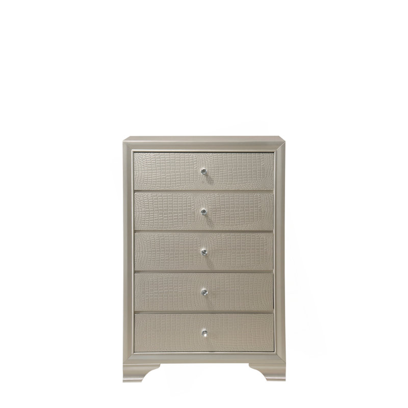 Superbe commode à cinq tiroirs au fini champagne avec des détails glamour pour l'élégance de la chambre à coucher.