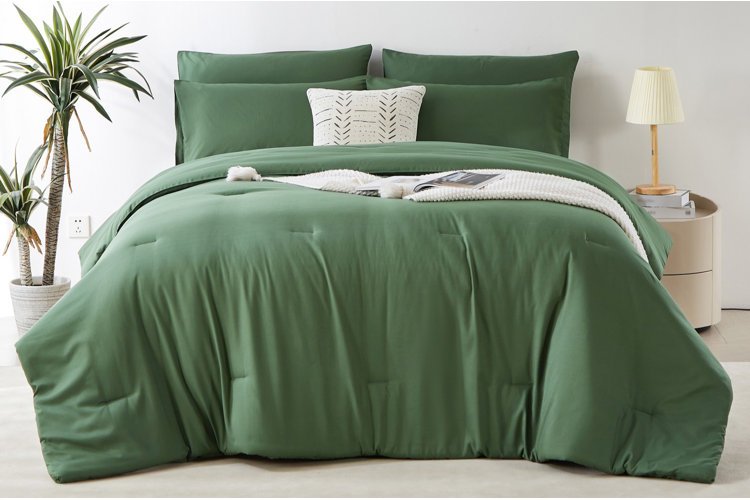 queen bed with soft green comforter and matching pillows in modern bedroom with standing plant and wooden lamp on nightstand