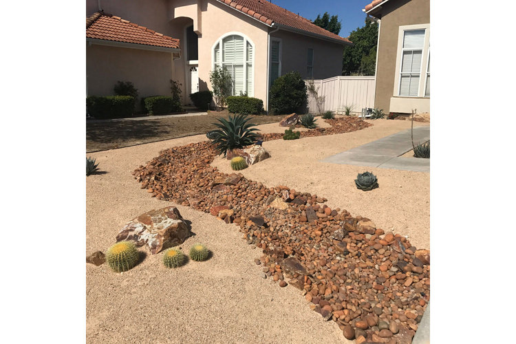 large dry sand front yard filled with a beautiful river of rocks and various succulents and cacti
