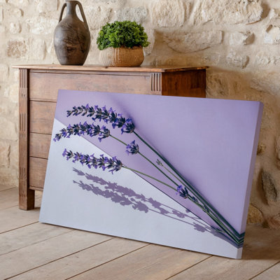 Toile, "Un arrangement délicat de fleurs de lavande s'appuie gracieusement contre un art mural sur fond mauve pastel, créant une toile sereine"