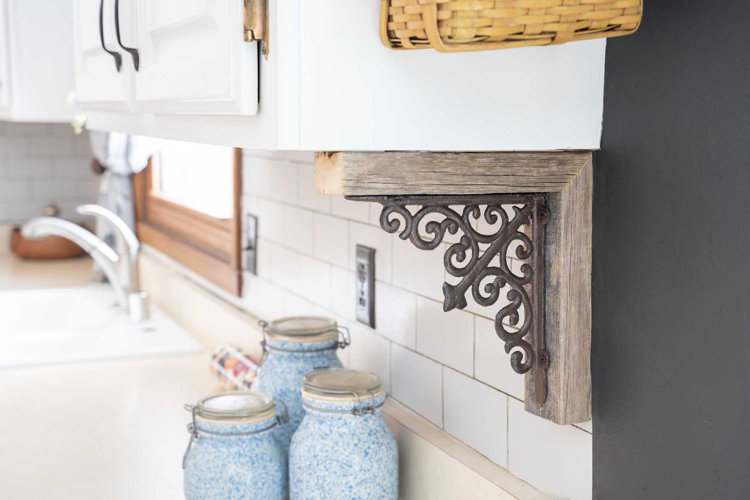 a wood carved corbel with a swirl design supporting a kitchen cabinet