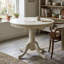 Ensemble de salle à manger 3 pièces en bois massif blanc lin, avec table ronde et 2 chaises à pied central en similicuir.