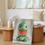 Toile, un adorable personnage de dinosaure assis avec une expression ludique tenant une grande tranche de melon d'eau-920226367